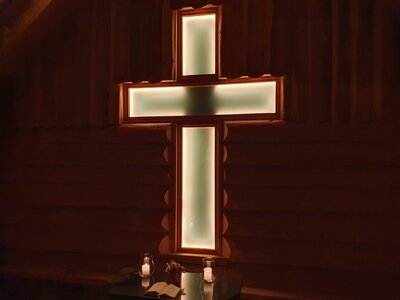 beleuchtetes Kreuz, ein Altar mit aufgeschlagenem Buch und zwei brennenden Kerzen